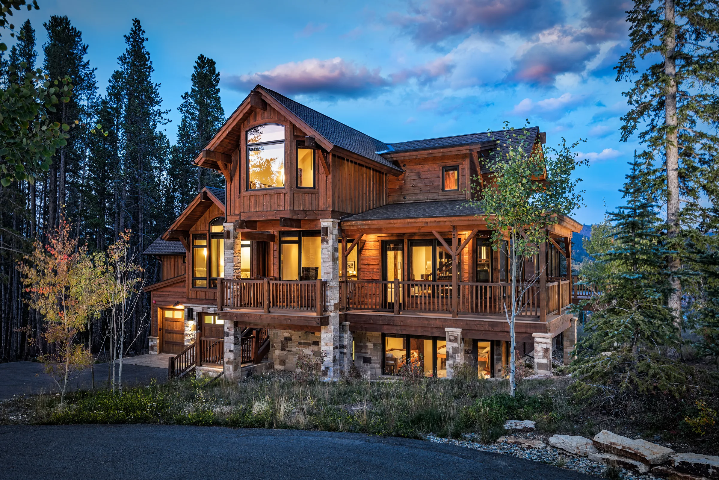 Timber mountain home with warmly lit windows among autumn trees at dusk